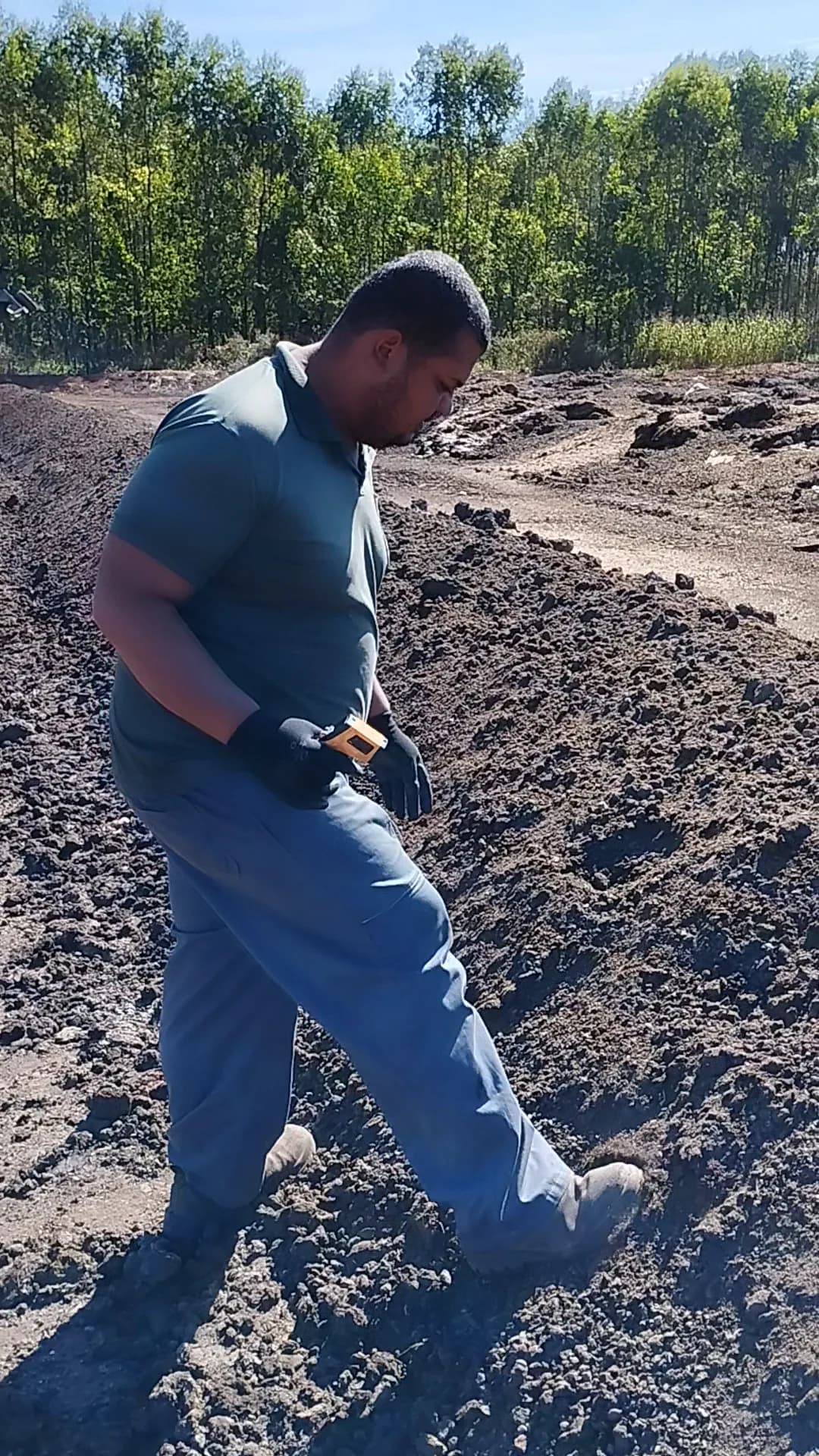 Operador caminha entre leiras de compostagem, com um instrumento portátil na mão.
