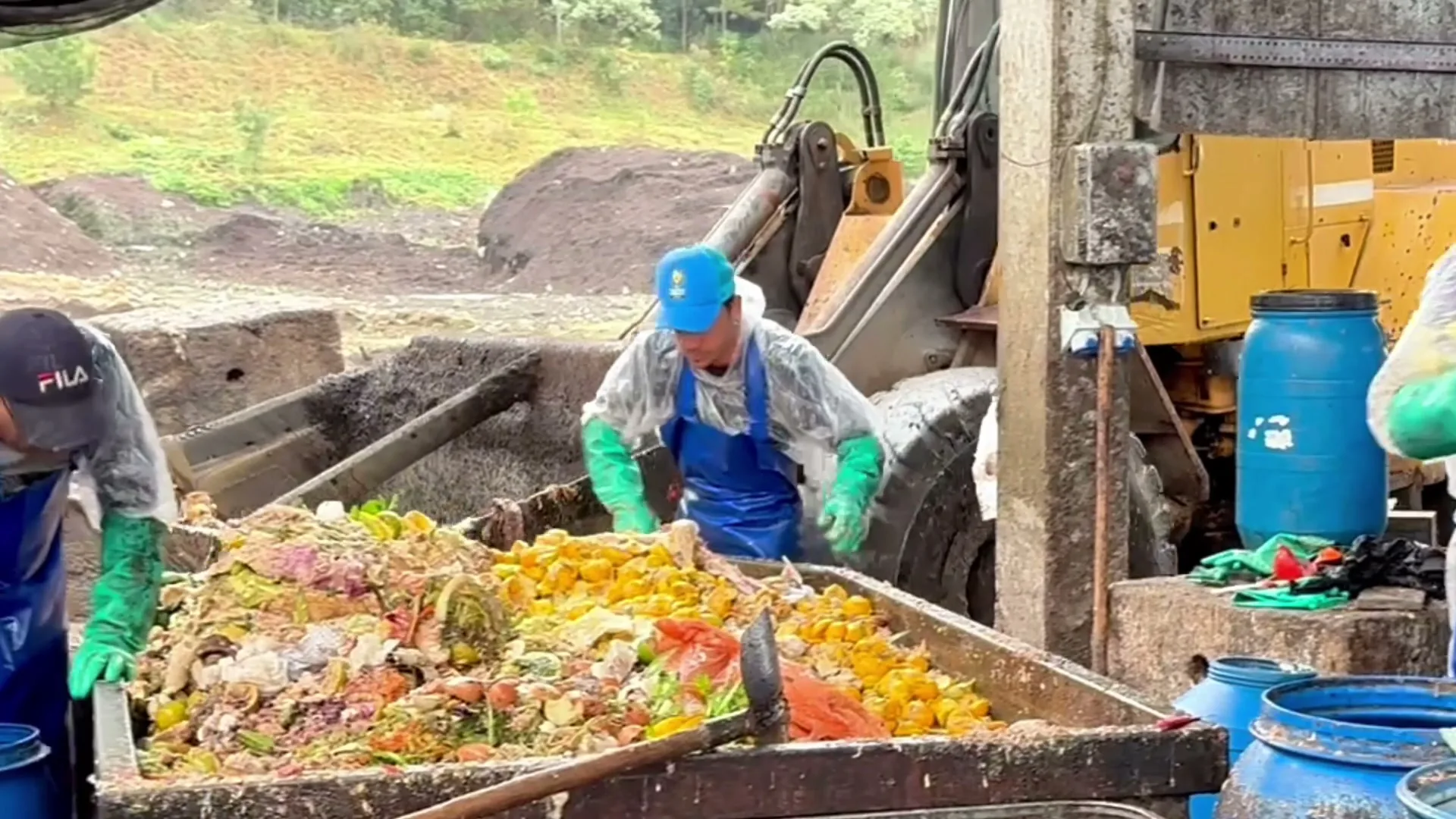 Trabalhadores separam resíduos de alimentos em uma mesa e esvaziam uma bombona azul.