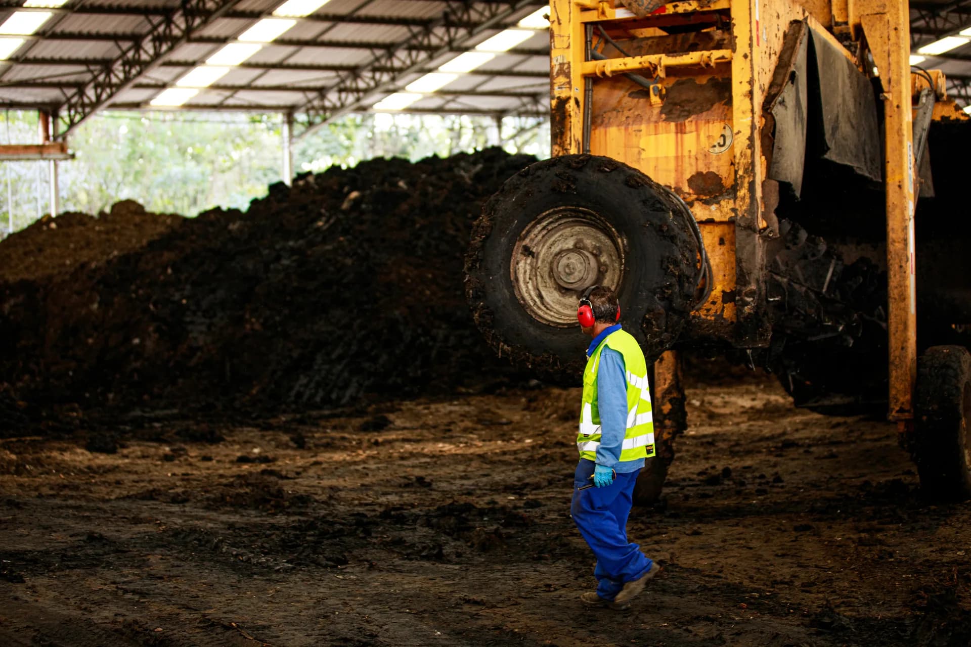 A worker in a reflective vest walks past machinery and compost piles.